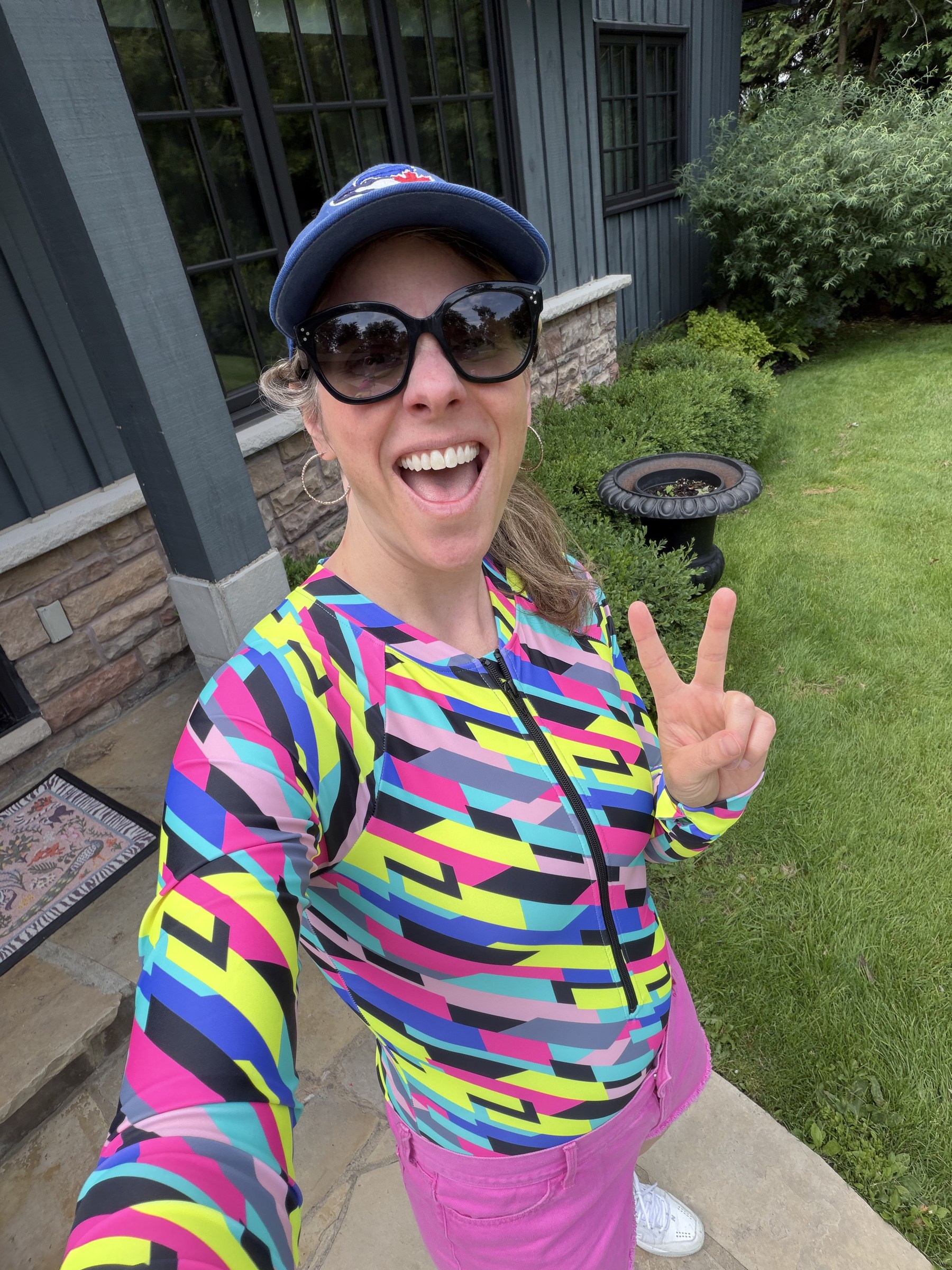 Quinn Simpson smiling in a vibrant geometric bathing suit and holding up a peace sign
